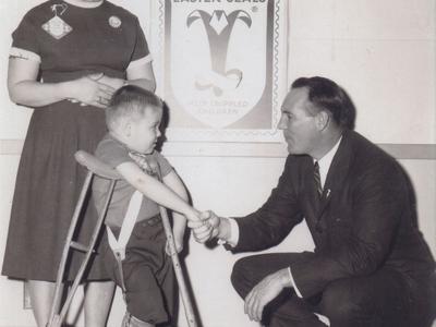 A man kneels down to shake the hand of a child in crutches.