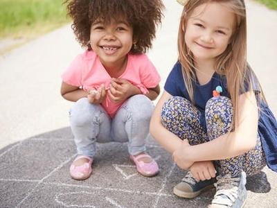 Two children smile at the camera as they sit outside.