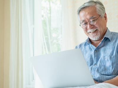 An older man smiles at his laptop.