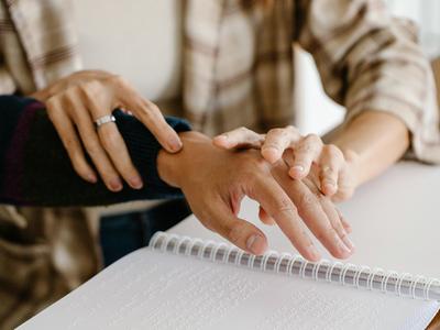 An image of two hands guiding a third across braille.